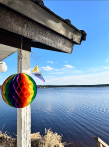 Kesäinen järvimaisema kuvattuna terassilta, kuvassa näkyy paperista taiteltu sateenkaaripallo